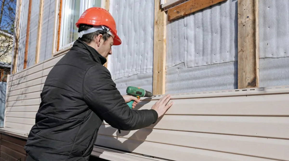 Siding replacement professional using a power drill to install new tan vinyl siding on a home exterior in Henderson, NV